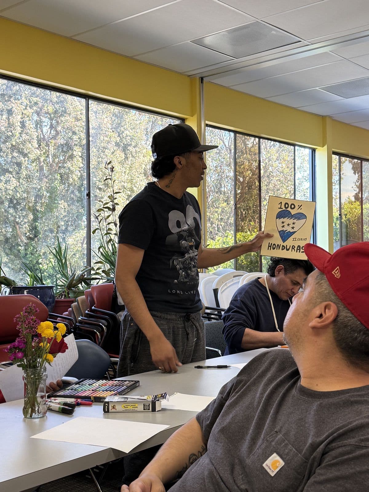 A resident standing to share his drawing of a heart filled with the Honduran flag, labeled “100% Honduras”