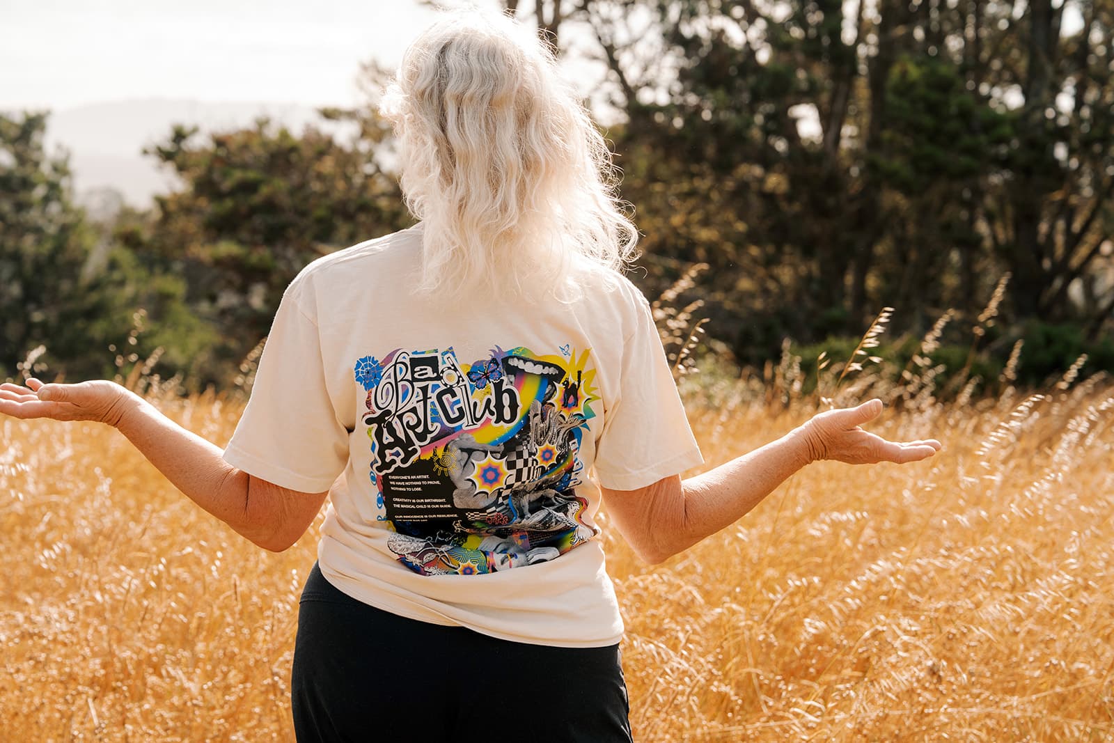 Man smiling in a black Bad Art Club tee in a golden field