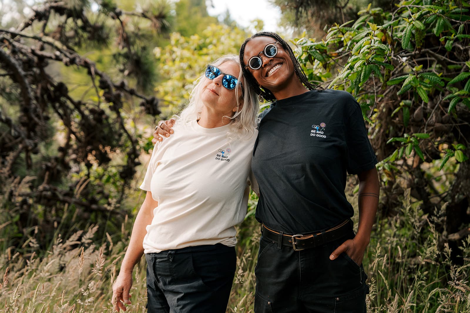 Two people arm-in-arm, wearing cream and black Bad Art Club tees from behind