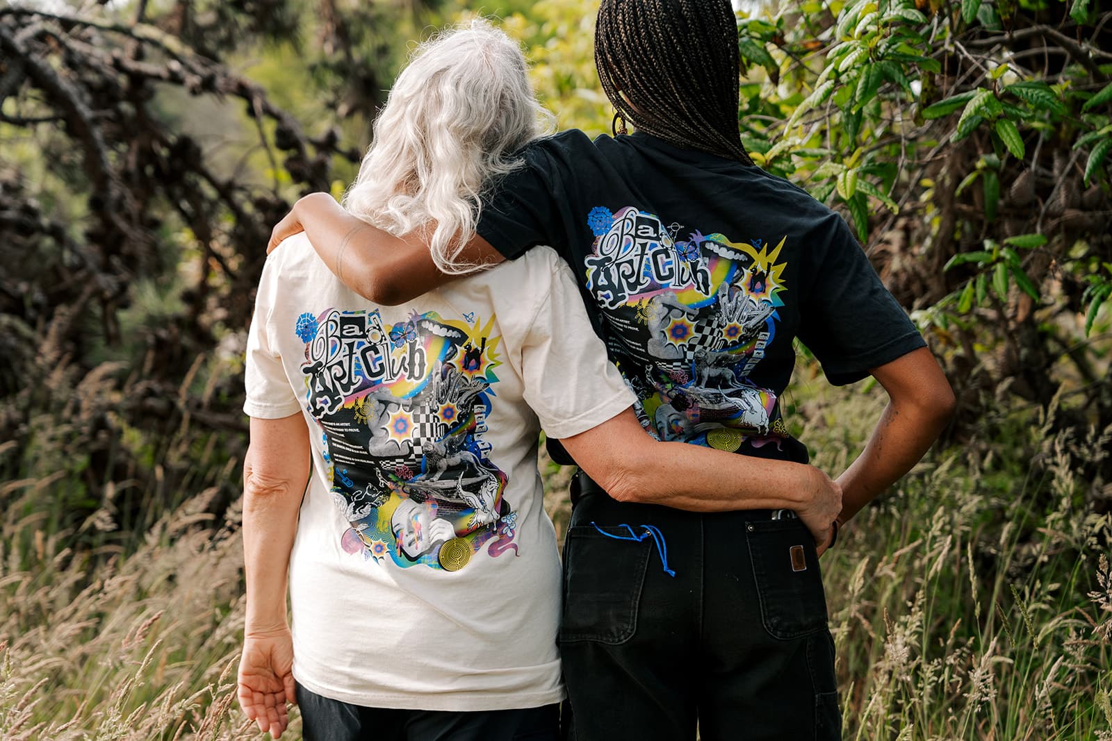 Two friends smiling together in cream and black Bad Art Club tees