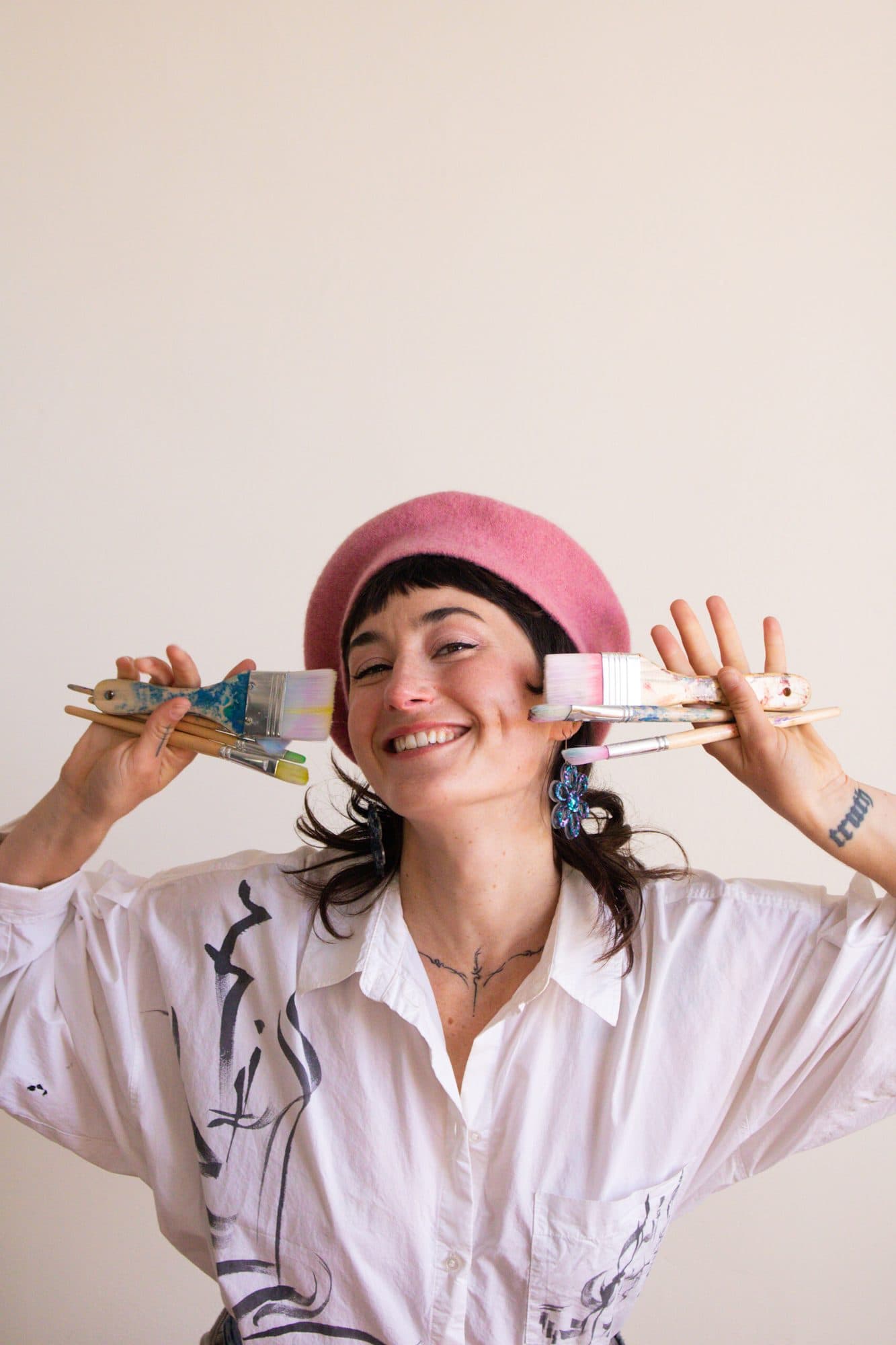 Julianne in a pink beret, holding a fan of paintbrushes to her face.