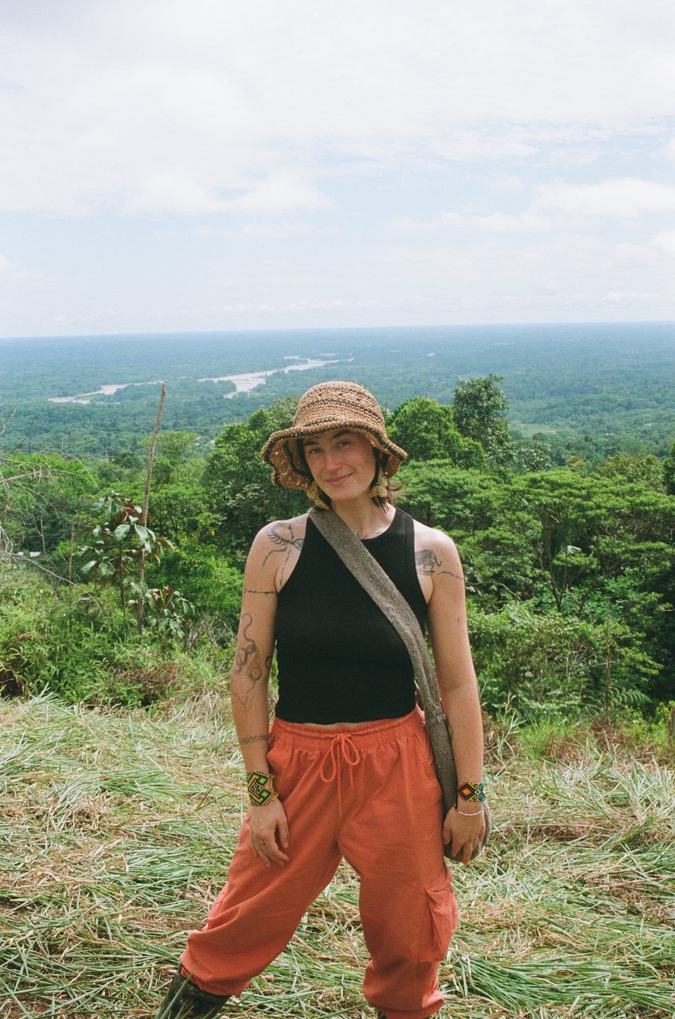 Julianne in a straw hat on a hilltop above a winding river and rainforest.