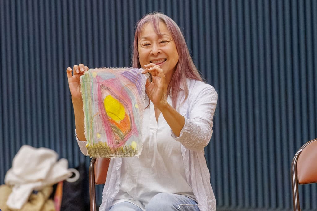A staff member with pink hair beams as she holds up her self-portrait artwork