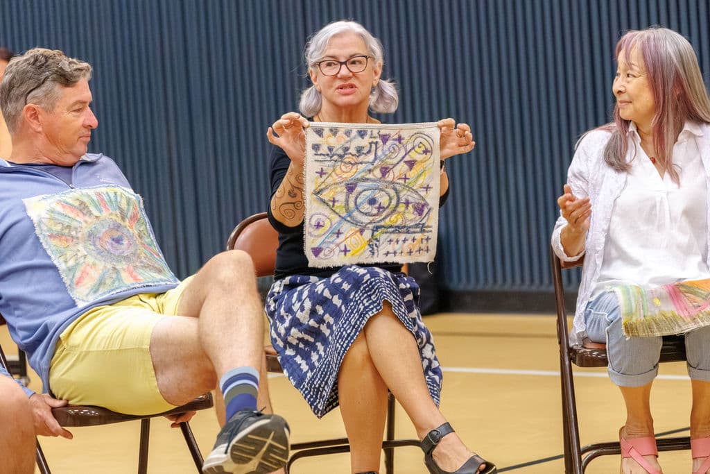 A staff member holds up an intricate self-portrait while sharing about it with the group
