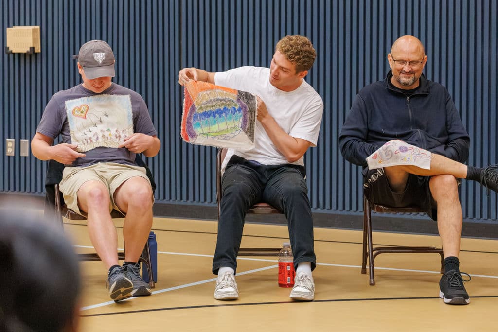 Three staff members seated in the circle, each holding and studying a self-portrait that isn't their own