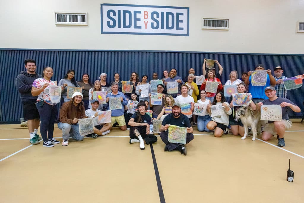 The full Hunt School staff holding up their self-portrait artworks in the gymnasium