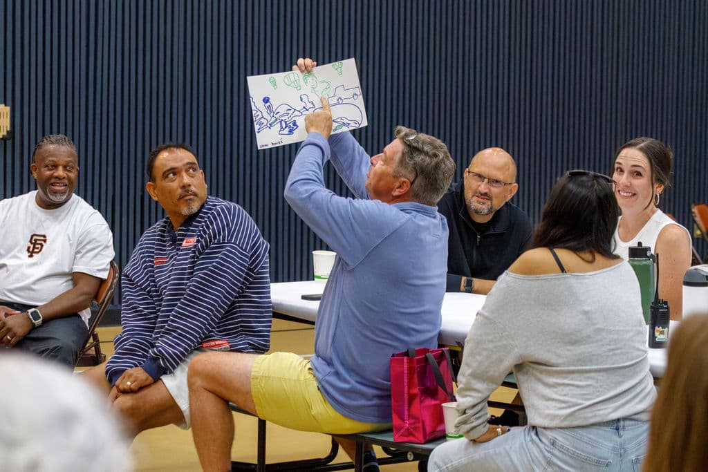 A man triumphantly holds up the group's collaborative drawing while his tablemates laugh