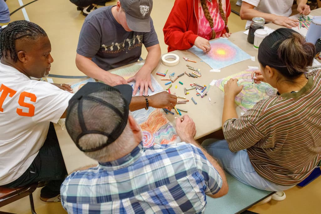 A group of staff working together at a table covered in pastels and self-portrait artworks