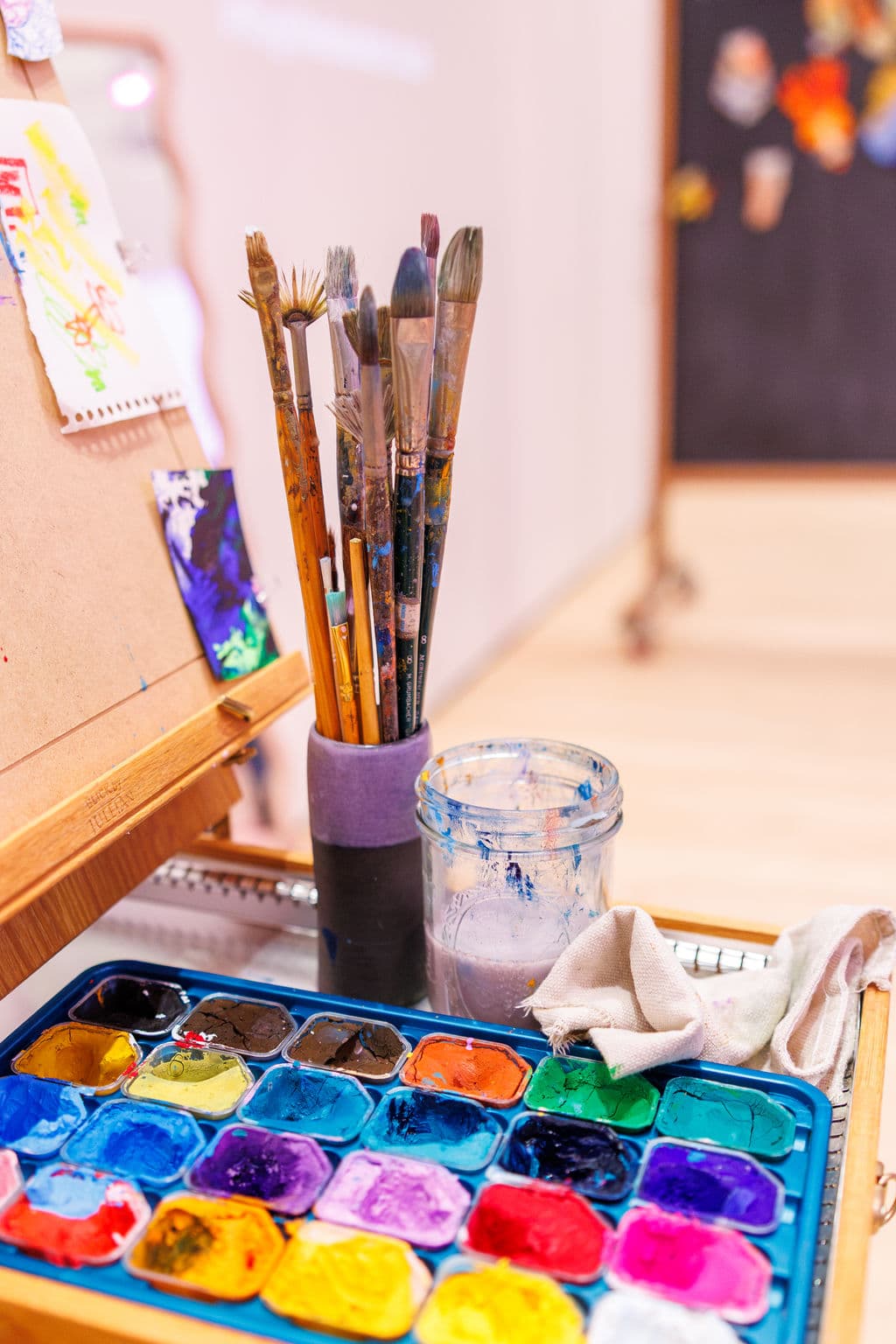 A jar of well-used paintbrushes alongside a full watercolor palette on a painting station