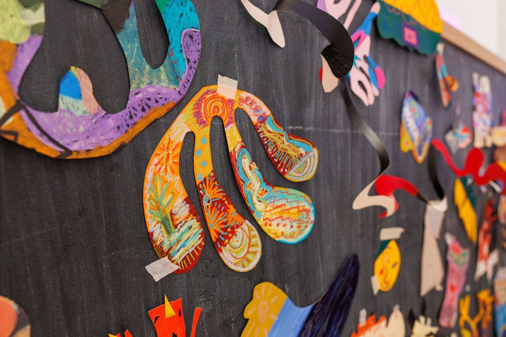 A close-up of the collaborative collage wall, thick with colorful cut and painted paper shapes layered on a dark background