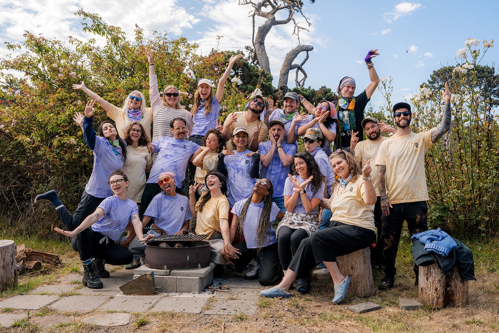 A large group of Bad Art Club participants in tie-dye shirts celebrating together outdoors, arms raised and laughing