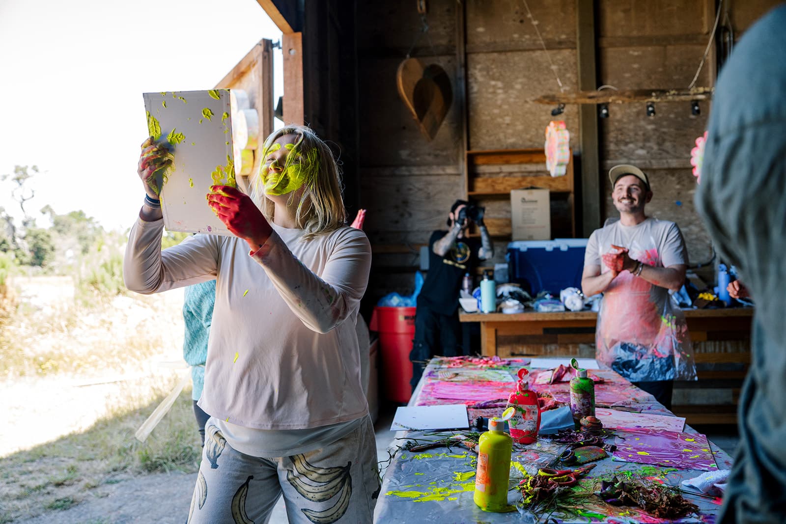 A person with neon paint on their face and hands, holding up a painting and smiling