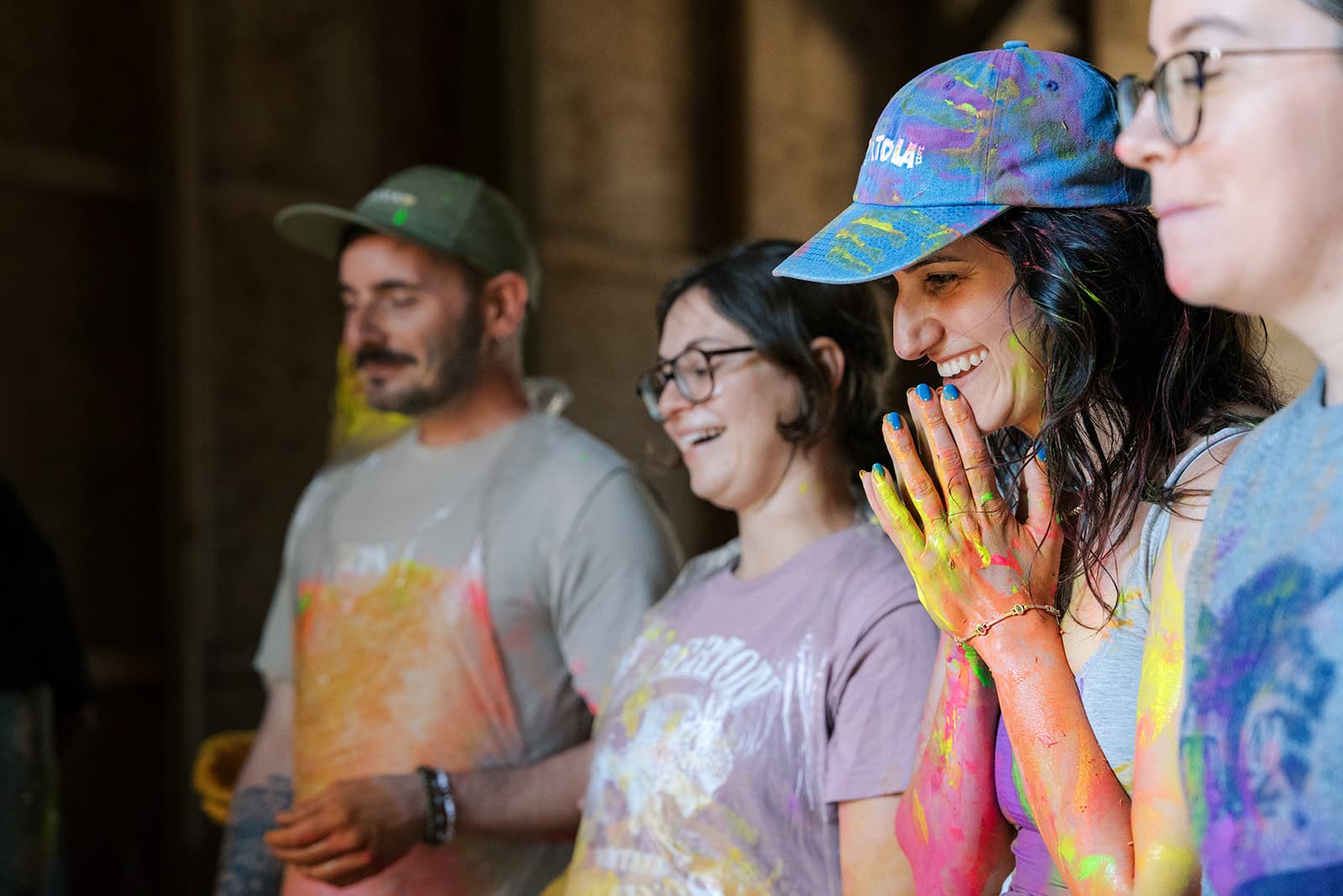 Four people laughing with paint all over their hands and clothes