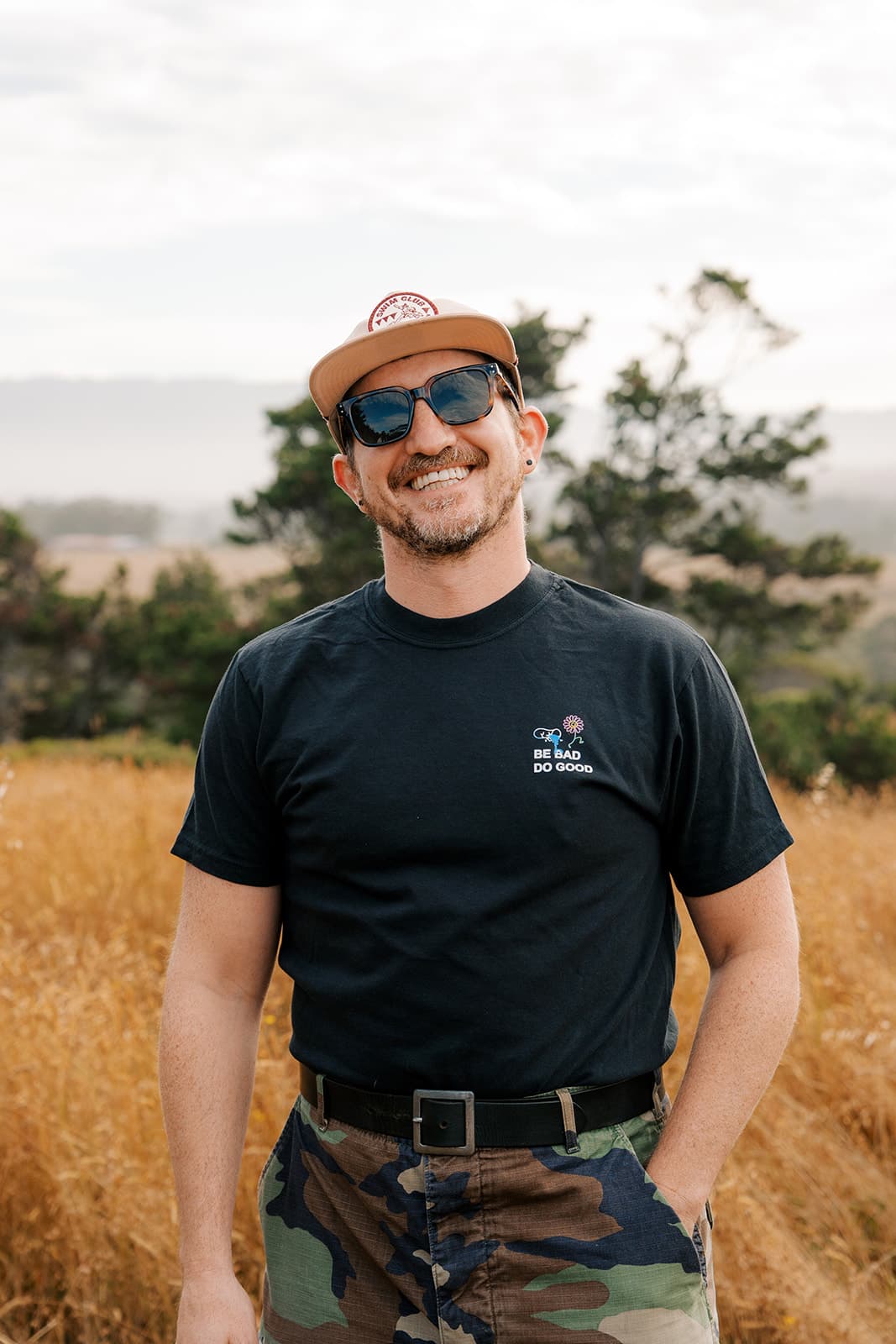 Man in a black Bad Art Club tee smiling in a golden field