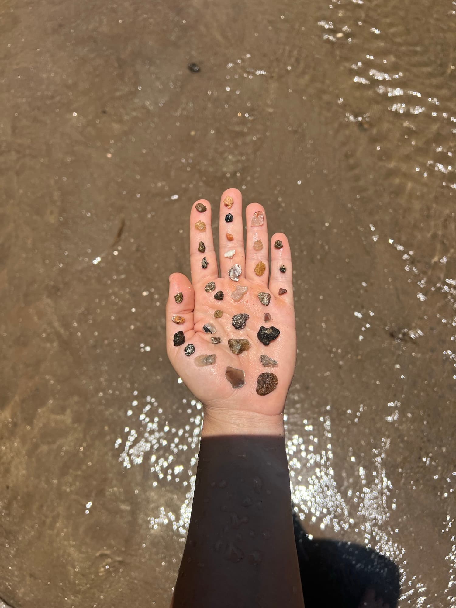 An open hand holding a collection of small river stones over the water.