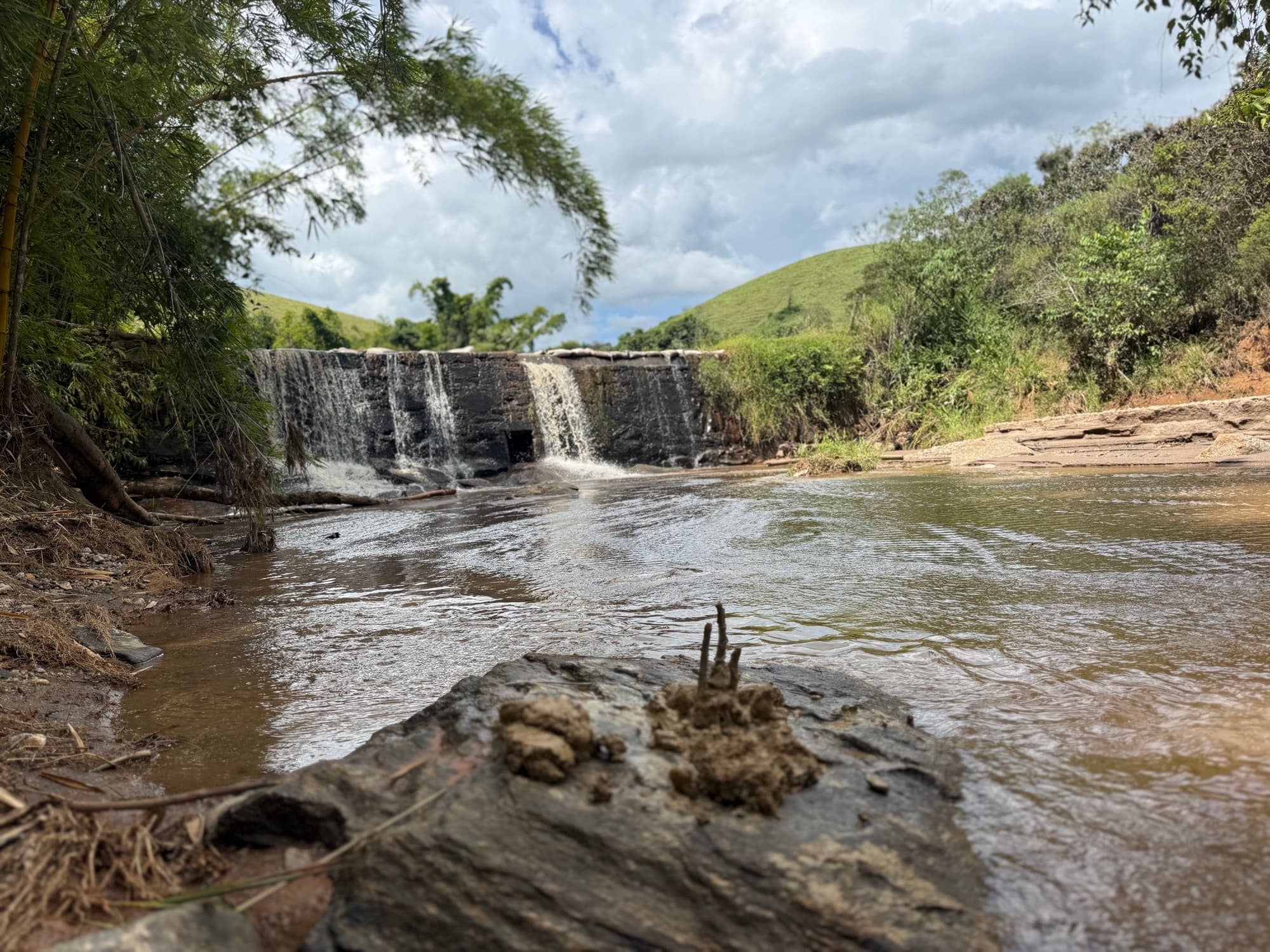 A river and small waterfall running through the forested farmland.