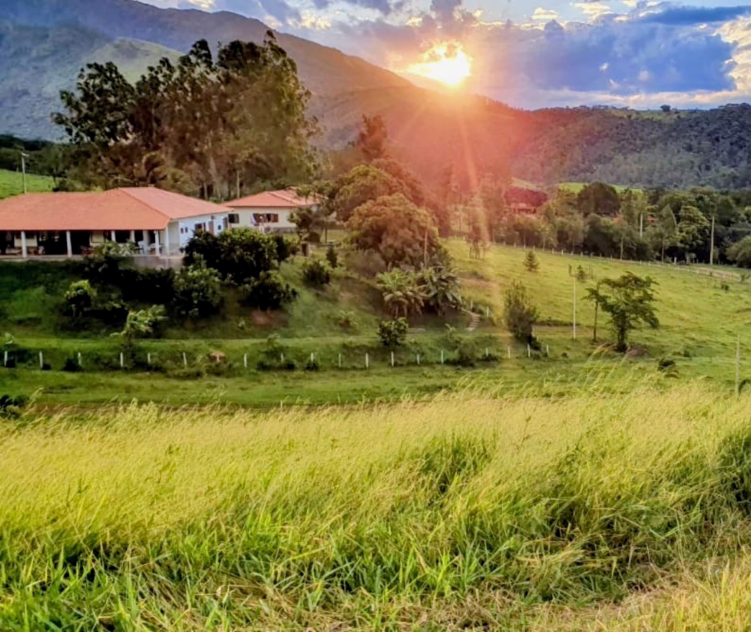 Sunset over the farmhouse and meadow, mountains behind.